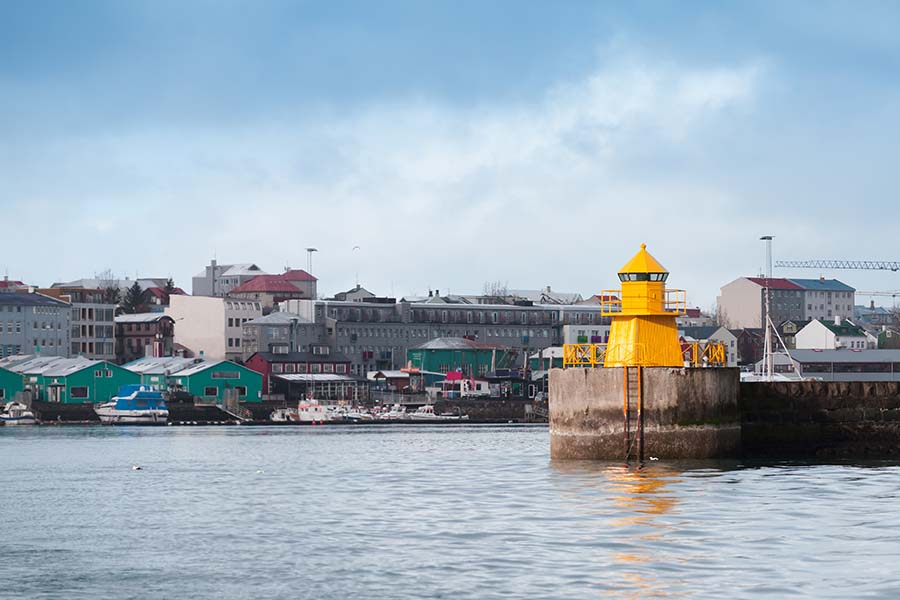 Yellow lighthouse tower on concrete breakwater, entrance to Reykjavik port